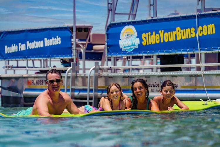 family of 4 floating on a lily pad beside double decker pontoon boat rental