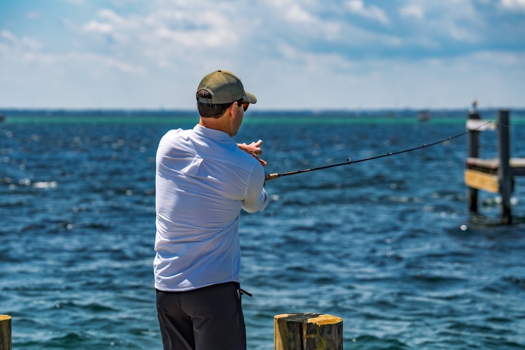 man casting a fish hook off a dock in the destin harbor