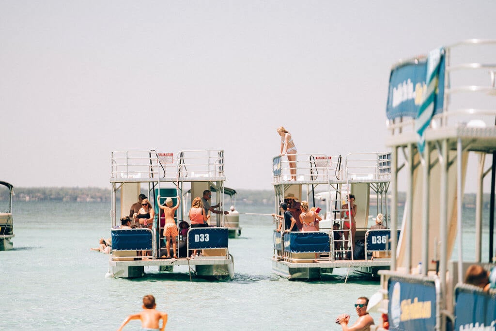 people standing on two double decker pontoon boats parked in the ocean by crab island