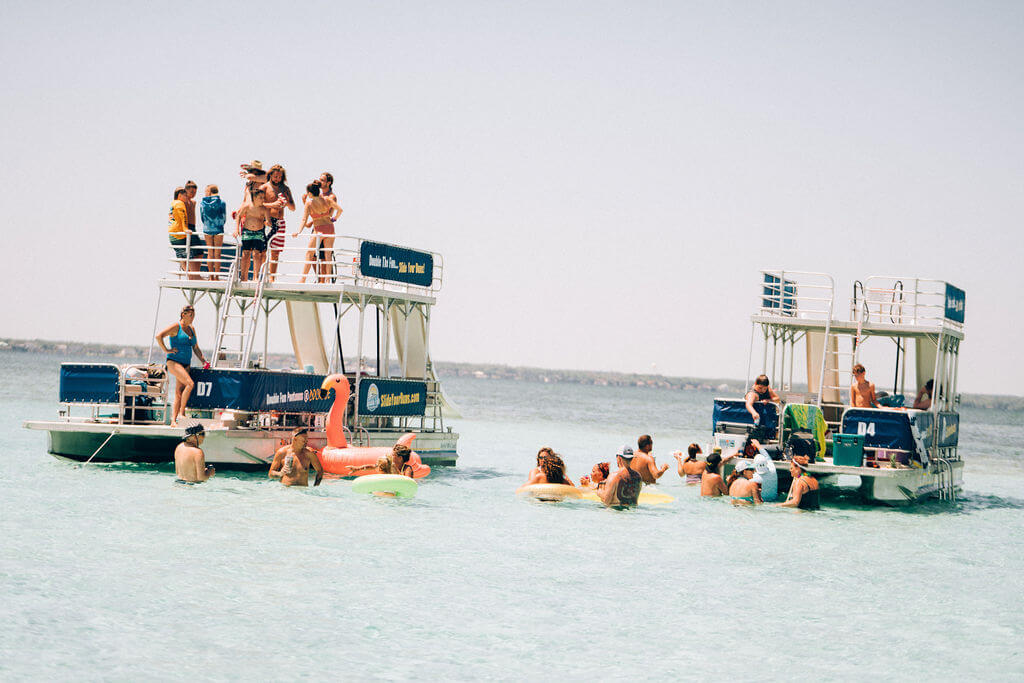 two double decker pontoon boats parked in the ocean with people swimming around them