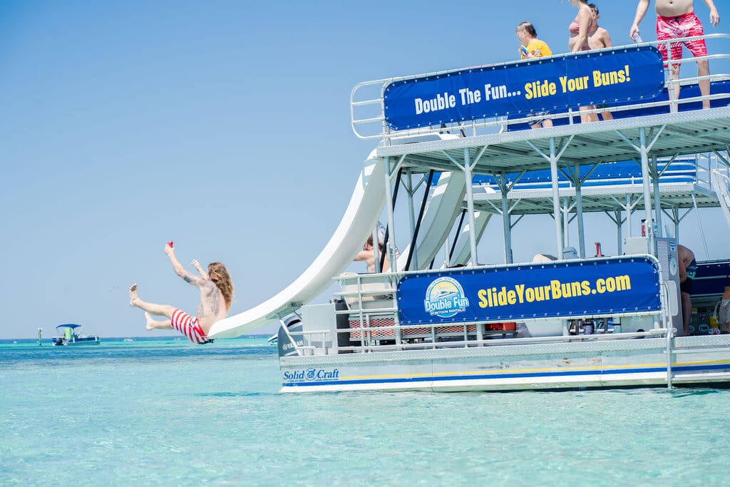 man sliding off one of the slides on a double decker pontoon boat into the ocean in destin, florida