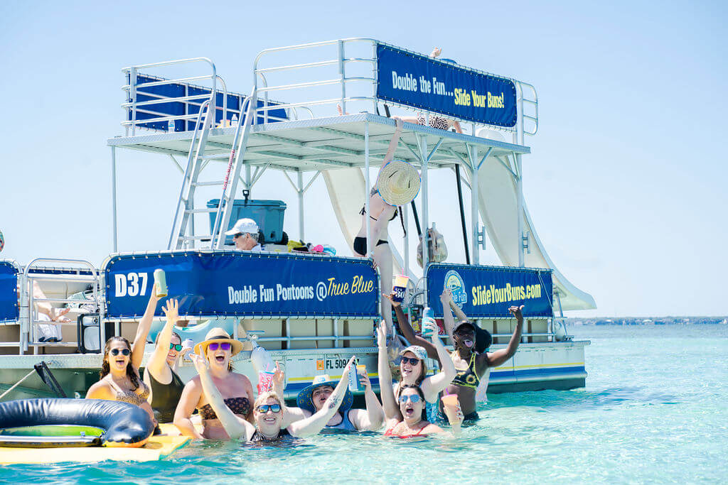 group of women raising their hands in the ocean in front of a double decker pontoon boat 