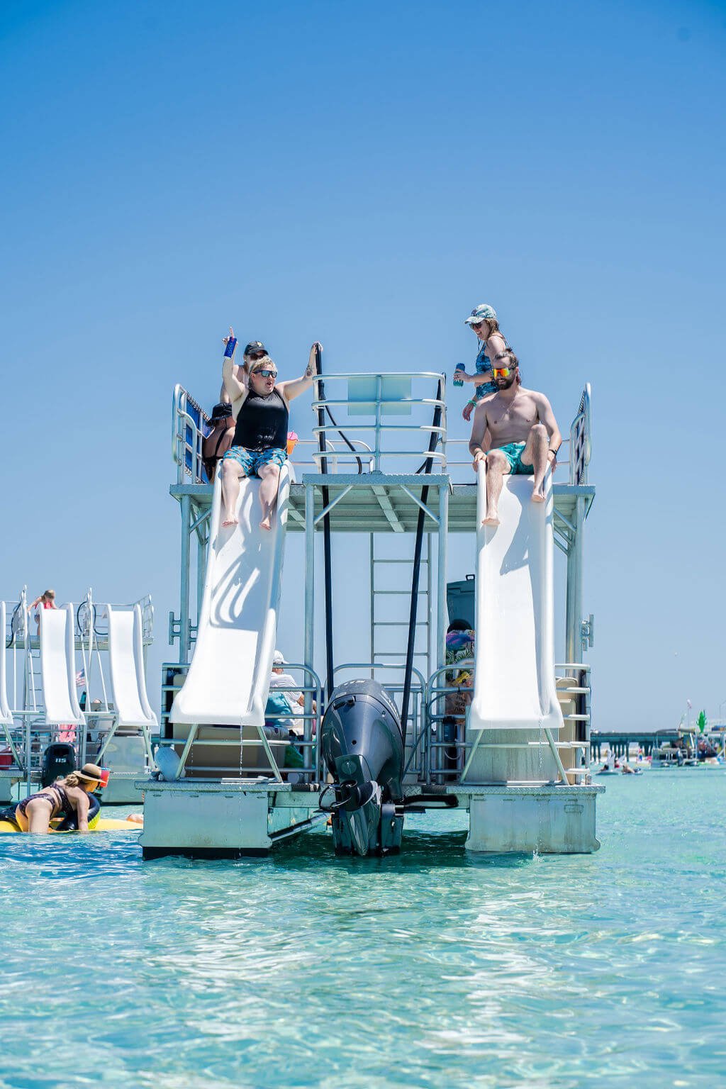 two people sliding off two waterslides on a double decker pontoon boat into the ocean