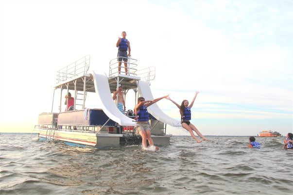 two people sliding into the ocean off of a double decker pontoon boat with two waterslides 