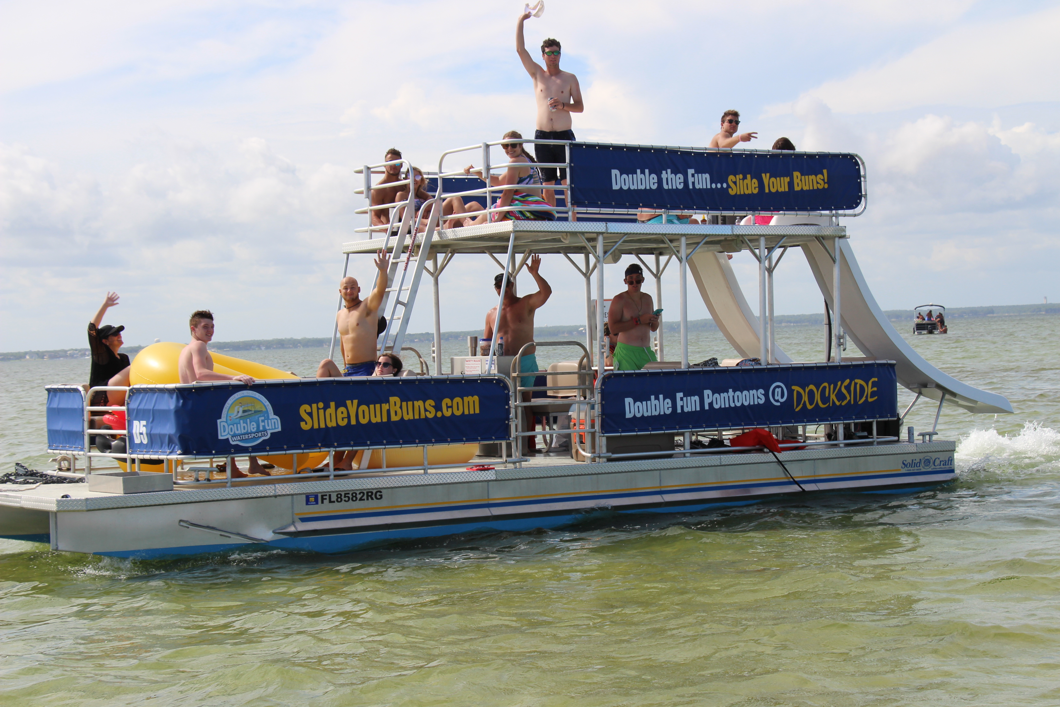 group of people enjoying a cruise through the ocean on a double decker pontoon boat with two waterslides
