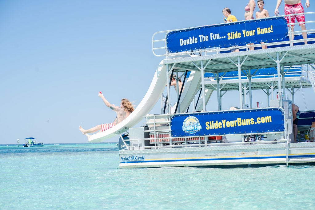 man sliding down a double decker pontoon boat slide by crab island in destin, florida
