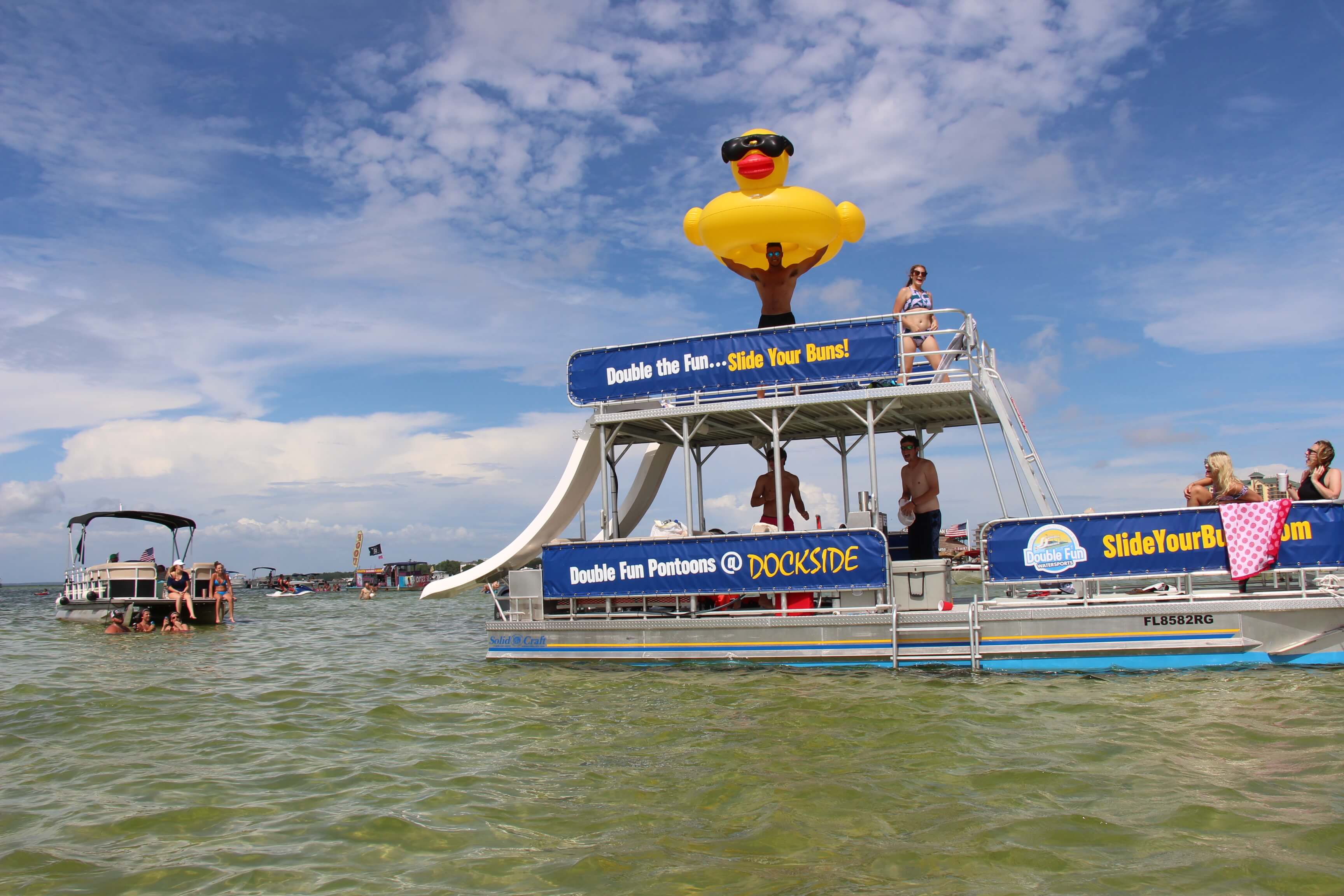 man holding a large rubber ducky float on top of a double decker pontoon boat in destin, florida