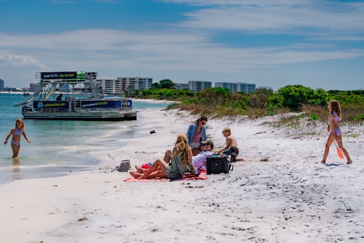 family and friends laying on destin beach with double fun pontoon in background