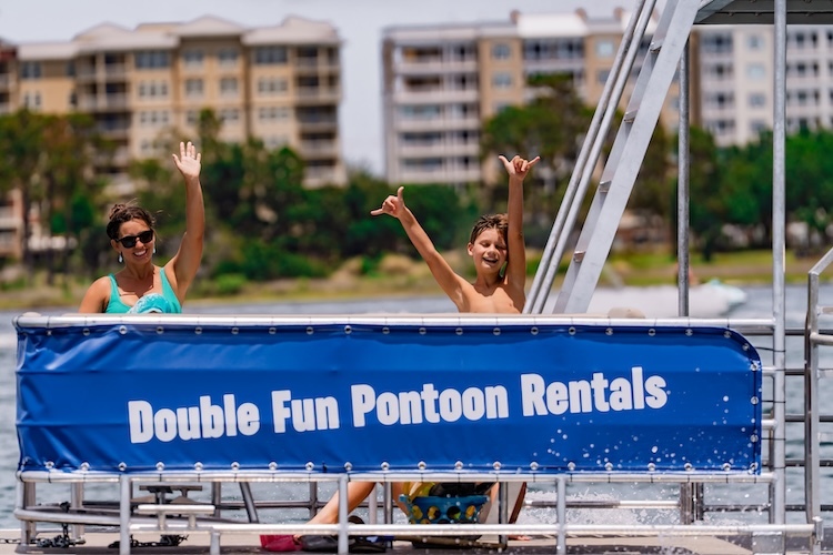 mom and child sitting and waving to camera from a cruising double decker pontoon boat rental in panama city beach fl